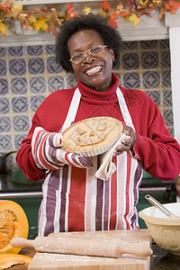 欧派厨房做万圣节招待和微笑的厨房里的女人厨师烘烤中年女子木板南瓜派女士食物假期乐趣背景