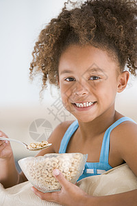 麦片碗里女孩年轻女孩在客厅里笑着吃麦片一个女孩健康饮食食物儿童混血儿食品饮食家庭谷物头肩背景