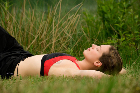 运动中的年轻青年在草原草地的草丛中休息黑发女士卷发女性微笑睡眠美丽绿色体操服场地背景图片