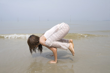 做瑜伽女孩在海滩上做瑜伽的亚洲女孩日出岩石运动身体海洋保健冥想日落卫生专注背景