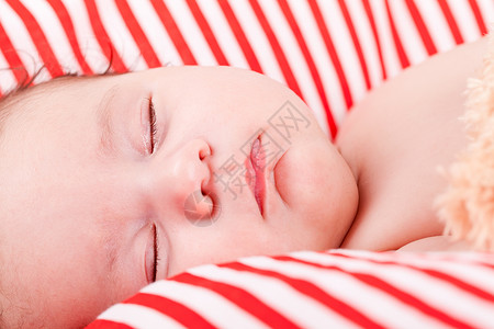 红色条纹枕头睡着的可爱小宝宝 在红色和白条纹枕头上孩子毯子童年生活女孩眼睛皮肤时间新生家庭背景