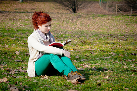 公园里的红长头发女孩在看书头发绿色读书季节裤子红色背景图片