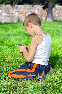 超然带移动电话的孩子学习小伙子细胞童年阳光晴天树木郊游场地汗衫背景
