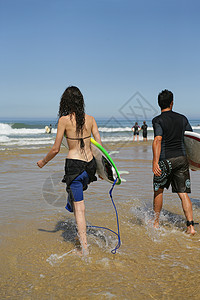 年轻冲浪者夫妻假期波纹冲浪男人趴板蓝色恋人黑发金子背景图片