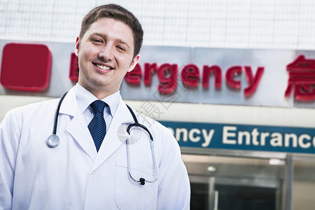 外出医院的年轻微笑医生肖像 背景中有急救室标志在后台专业文字露齿灾难权威情况头肩职业聚焦水平背景图片