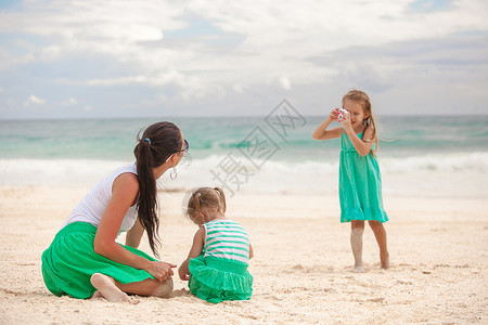 小女孩在沙滩上给妈妈和姐姐照相放松高清图片素材
