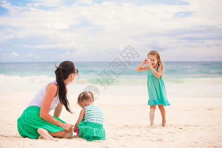 小女孩在沙滩上给妈妈和妹妹拍照片绿松石高清图片素材