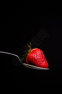 红原食物草莓 在黑背景的银勺子上背景