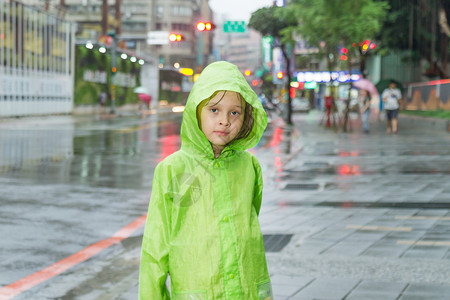 雨中行走孩子年轻女孩站在雨中 穿着绿色雨衣外套天气雨量女性季节微笑街道眼睛树木倾盆大雨背景