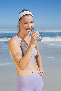 海洋补水运动快乐的金发金发美女在海滩上喝水文胸护理身体假期晴天紫色女性瓶子微笑锻炼背景