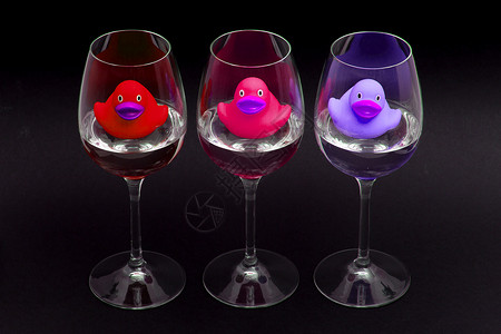 葡萄酒杯中的红 粉色和紫色橡皮鸭背景图片