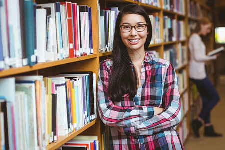 微笑的学生靠在书架的对面大学生知识女孩女士学校大学快乐校园双臂混血双臂交叉高清图片素材