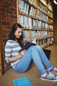 坐在地板上坐在图书馆阅读书墙壁对面的微笑学生文学女士休闲学校高等教育大学生校园知识混血快乐坐着高清图片素材