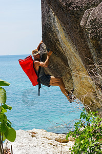 一个坚强而快乐的人 带着小屋和红色的海袋在海上攀登高高的岩石顶峰挑战远足石头风险悬崖勇气行动动机登山活动高清图片素材