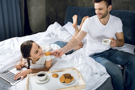 床和早餐男子喝咖啡时 妇女在床上使用笔记本电脑男朋友两个人微笑饮料托盘男人技术女士食物咖啡背景