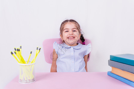 穿着校服的可爱快乐小女孩的肖像头发孩子白色学校幼儿园铅笔桌子微笑女孩椅子脸高清图片素材