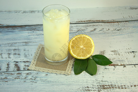 清爽柠檬装饰白色木桌上放着一个玻璃杯 上面放着清爽的果汁和冰块 放在纺织品架上 用叶子切了一半柠檬玻璃食物风格假期海报装饰物品热带树叶季节背景
