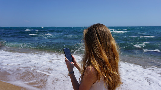 使用移动电话 海滩和海背景的近身检查一名女性女士天空娱乐潮人技术细胞地平线假期海洋互联网信息高清图片素材