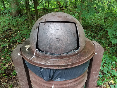 森林中带有推标的生锈棕色金属垃圾桶背景图片