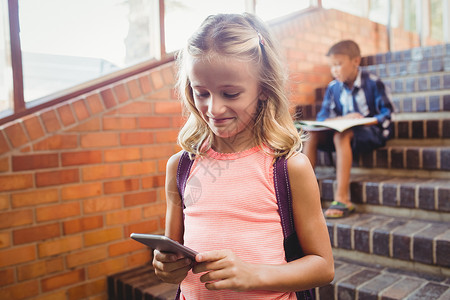 可爱的小女学生在看她的智能手机滚动男性红砖男生金发女郎休闲快乐沟通服装学校背景图片