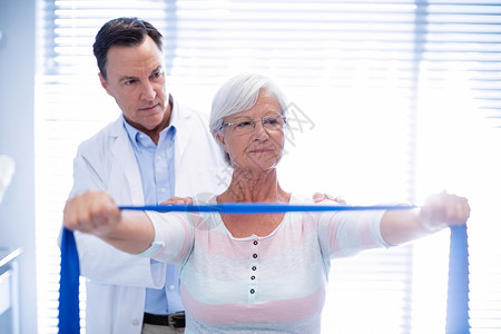 男性理疗师给高龄妇女做肩部按摩外套医学专家治疗师老年服务访问按摩师脊椎骨科背景图片