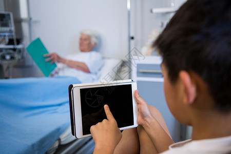 男孩使用数码平板电脑 而高级病人在阅读背景书籍时使用数字平板电脑微笑高清图片素材