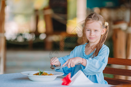 可爱的小女孩在户外咖啡厅吃晚饭果汁勺子食物幸福婴儿酒店早餐午餐面条桌子饥饿的高清图片素材