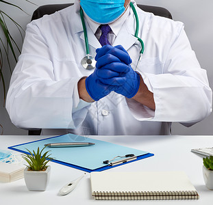 穿白大衣和蓝色乳胶手套的男男性医生坐在Whit治疗师保健笔记本医院实验室咨询卫生病人桌子办公室药品高清图片素材