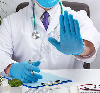 身穿白色医疗大衣的医生坐在棕色礼服的桌子上手势诊所职场注意力手套男人笔记本成人药品治疗师棕榈高清图片素材