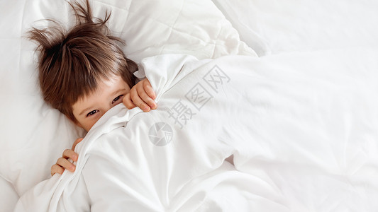 喜床边框小孩小可爱躲在床上 被吓坏的男孩醒来并偷窥出来婴儿手表欢乐毯子幸福就寝孩子横幅乐趣衣冠背景