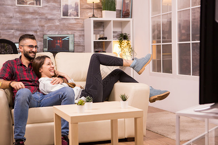美丽的年轻夫妇在沙发上放松 同时观看电视上的电影场所房间夫妻娱乐恋人电视节目程序房子长椅公寓背景图片