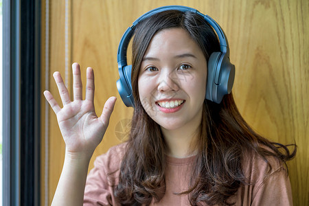 亚裔年轻女性在制作影片时挥手打招呼疾病预防搜索相机耳机人士视频博客营销传染病社会责任感高清图片素材