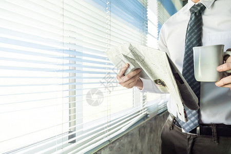 商务人士阅读报纸和咖啡杯 同时站在办公室的窗户边站一扇窗户上老板高清图片素材