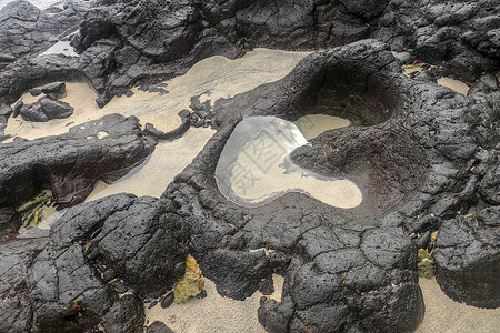 黑色沙子底部有白色沙子的岩石凹陷处充满了海水 在印度洋海岸巴厘岛印度尼西亚的熔岩床中挖掘出的小池塘 潮水在黑色岩石中挖出了小湖海岸线天堂背景