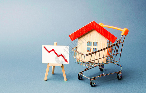 红色地产海报购物车中的房屋和带有向下红色图表箭头的支架 房地产市场的下跌 价值或成本降低的概念 低流动性和吸引力 便宜的租金或购买成本背景