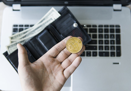 钱包硬币男人手里拿着金色的比特币硬币 背景是笔记本电脑 还有带钱的皮钱包 手持加密货币的人 虚拟货币 商业 商业 交换 数字货币网络购物背景