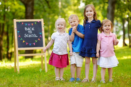 生完孩子四个兴奋的小孩 在黑板旁边学生同学旗帜木板公园粉笔花环幼儿园团体女孩背景