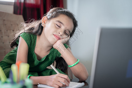 女童在笔记本电脑前的在线课堂上睡觉 — 在 covid-19 或锁定期间 从远程学习或在家进行在线教育的疲倦孩子的概念背景图片