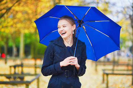 蓝色伞秋天或春季下雨日 在卢森堡巴黎花园的卢森堡花园中带蓝伞的年轻女子季节园艺女孩花园预报橙子女士沉淀树叶公园背景