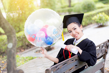 穿着学术服和学校服装的年轻快乐女毕业生肖像学习成人微笑证书女士研究生仪式气球文凭长袍学术的高清图片素材