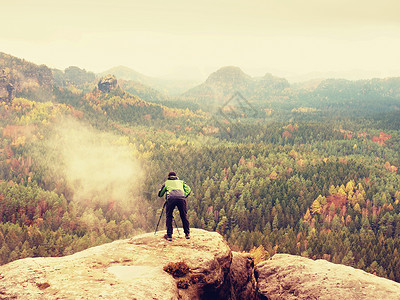 带相机的徒步旅行者在三脚架上从岩石山顶拍照 边缘照片风景的单独摄影师天空夹克登山服远足者太阳湿度条件天气爬坡光照背景图片