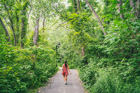 在 COVID-19 爆发的自我隔离检疫后 在自然森林公园女孩的户外夏季散步享受户外自由 走在森林小径路径的红色礼服的妇女去高清图片素材