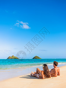 海滩度假情侣在美国夏威夷瓦胡岛拉尼凯的夏威夷热带海滩上放松享受日光浴 美国民众暑假躺在沙滩上晒太阳背景图片