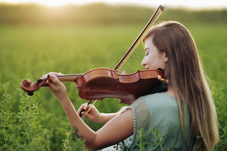 小提琴演奏时头发松发的浪漫女人 大自然的日落光旋律晴天交响乐艺术小提琴家女孩女性日落制造商夕阳背景图片