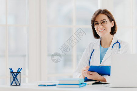女医生在特殊表格上开处方 在私人诊所工作 穿着白色医疗礼服 准备看病 在工作场所摆姿势 微笑的医生或医务工作者拿着剪贴板女性高清图片素材