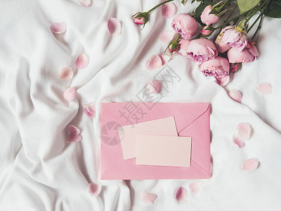 玫瑰信封玫瑰和花瓣在压碎的白色白织物上 自然优雅的装饰品信封折叠花束被单纺织品植物群植物粉色名片织物背景