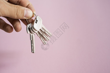 男士手拿着一组粉红色背景的钥匙 房地产经纪人为客户提供公寓钥匙 专注于按键 房地产经纪人手中的一串钥匙住宅成功销售抵押女士住房商家高清图片素材