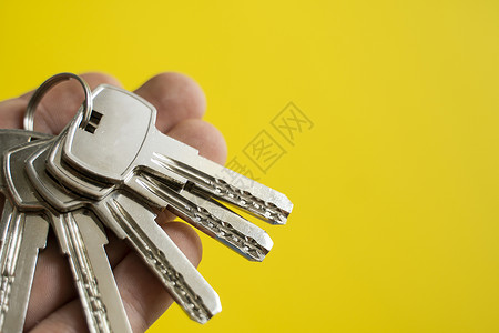男士手拿着一组黄色背景的钥匙 房地产经纪人为客户提供公寓钥匙 专注于按键 房地产经纪人手中的一串钥匙房东建筑成功代理人销售女士家房子高清图片素材