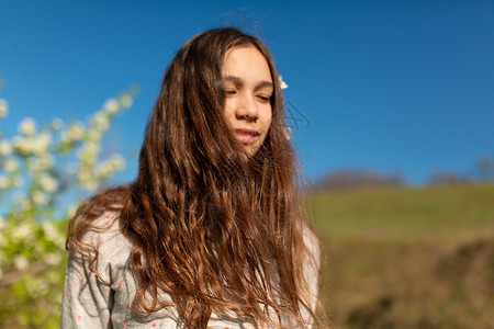 在一个盛开的春季绿花园里 一个年轻美丽的少女女孩的肖像头发冒充黑发公园洗发水情感季节晴天女士花园树高清图片素材