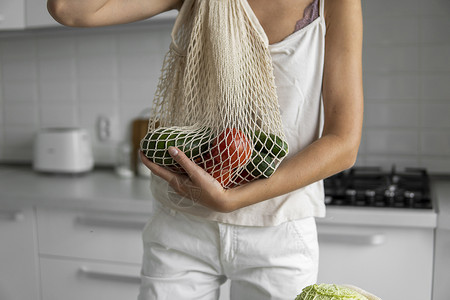 女人手拿着装有蔬菜和水果的可重复使用的购物袋 零废物和无塑料概念 女孩拿着带蔬菜的网眼棉购物袋 生态杂货农业网袋购物纺织品浪费回背景